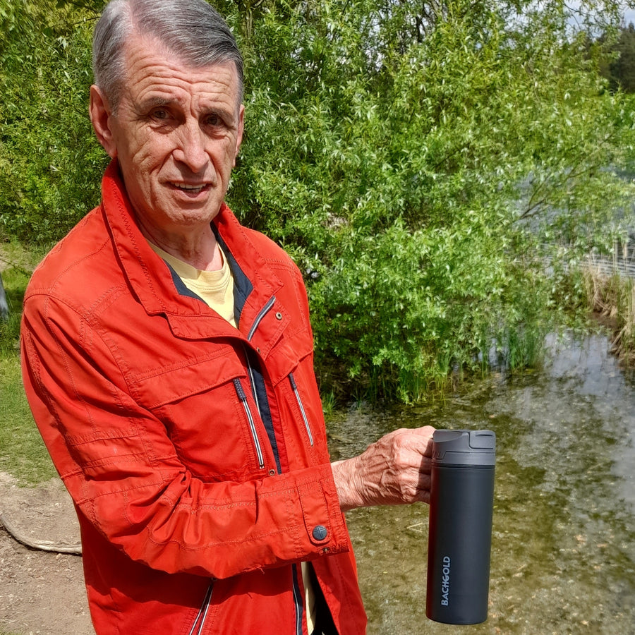 Man with red jacket holding black Bachgold® Selfpress Water Filter near a lake