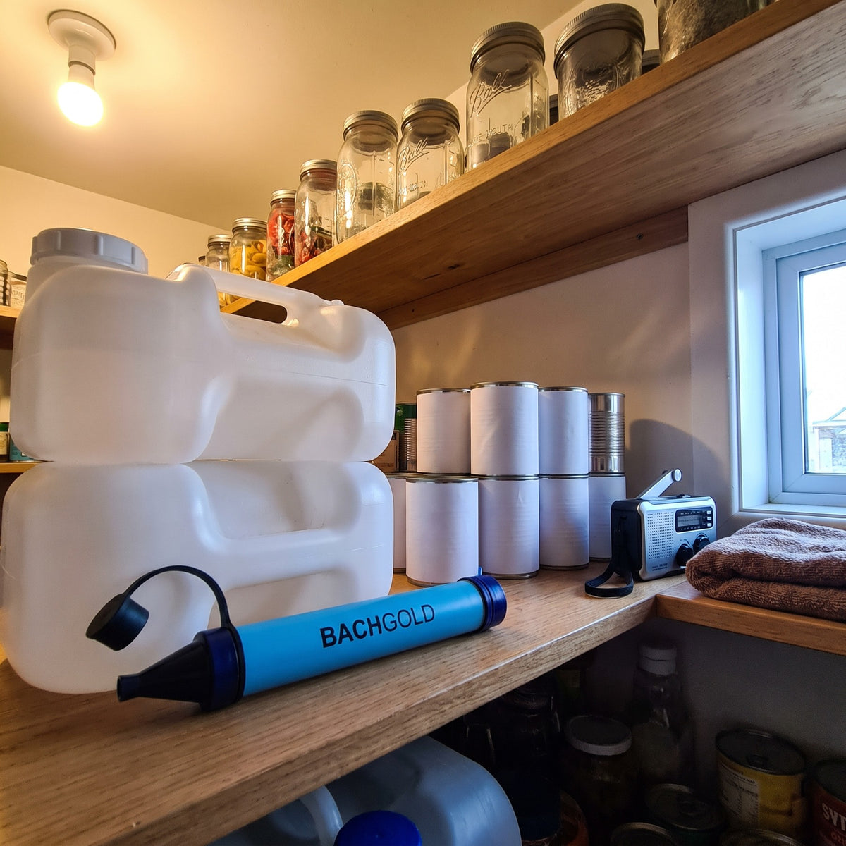 Bachgold Straw Wasserfilter liegt griffbereit im Vorratsschrank neben Wasserkanistern, Konserven und einem Kurbelradio