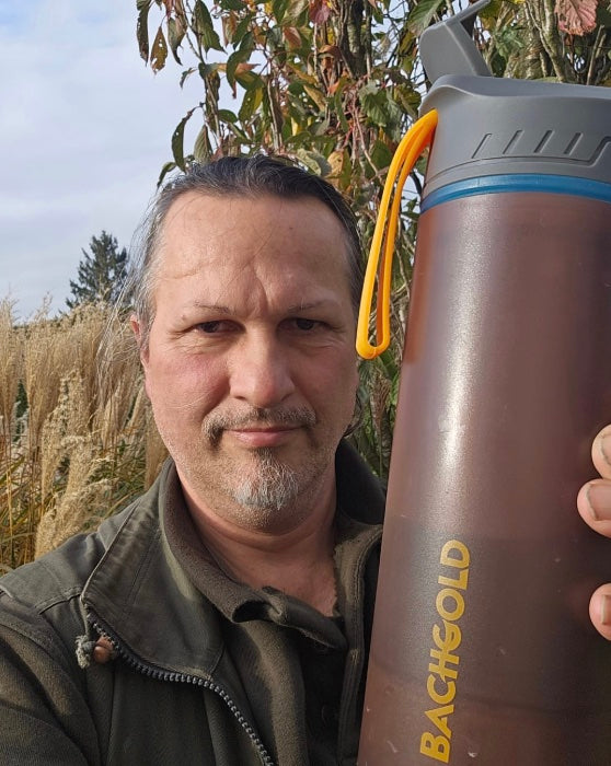 Mann mit Bachgold Flasche in herbstlicher Landschaft