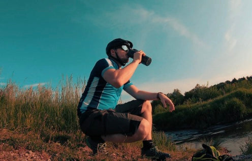 Radfahrer trinkt in der Pause am Flussufer