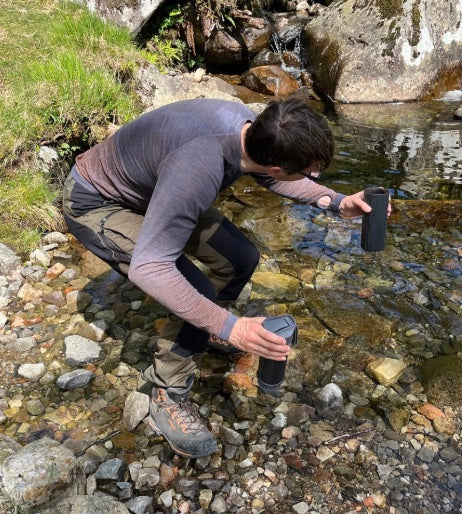 Mann füllt am Bach zwei Flaschen mit Wasser