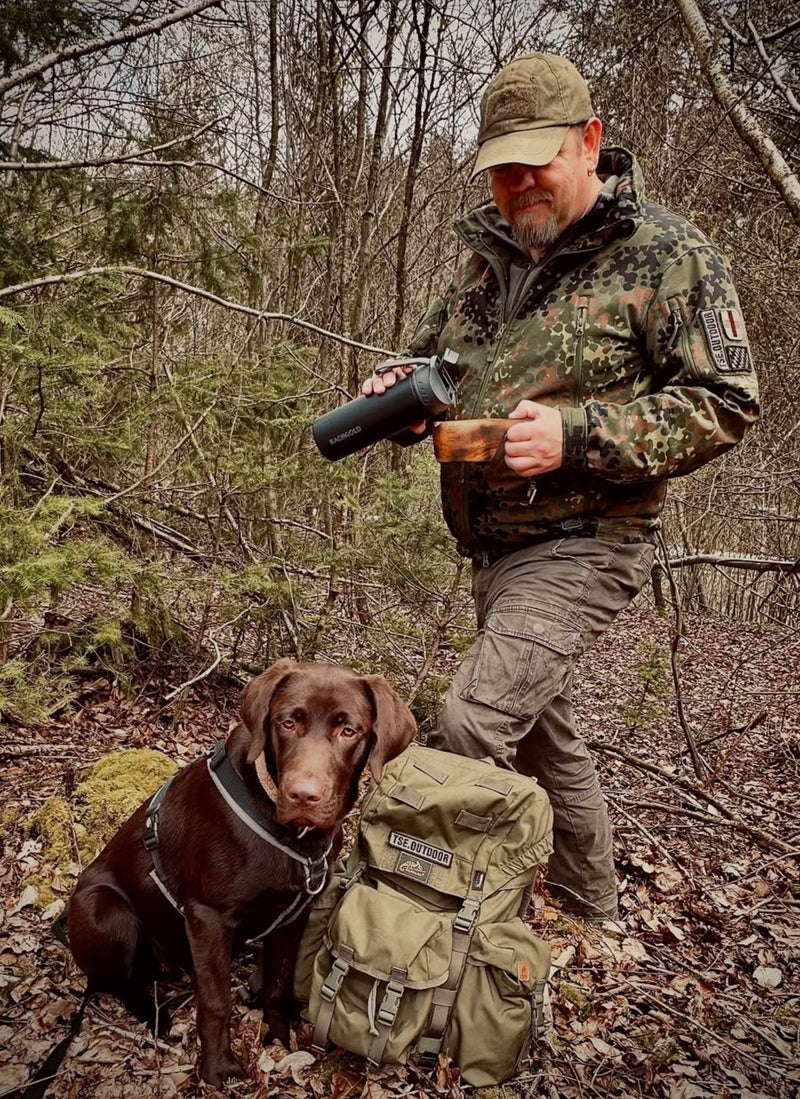 Wanderer mit Hund und Rucksack im Wald, Flasche in der Hand