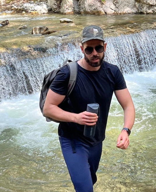 Wanderer mit Rucksack und Flasche vor einem Wasserfall